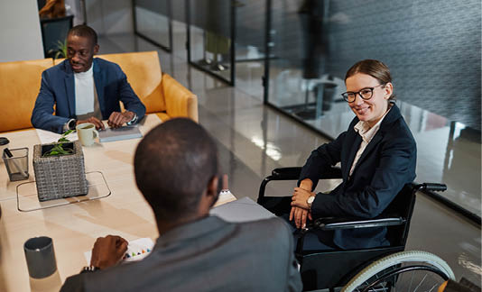 Portrait of successful businesswoman using wheelchair at meeting and talking to group of colleagues in modern office space