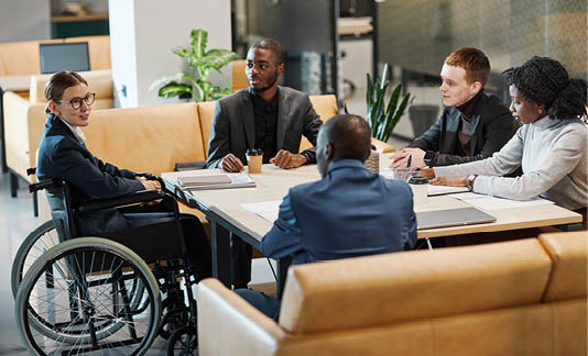 Full length portrait of successful businesswoman using wheelchair at meeting and talking to colleagues in modern office space
